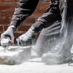 Person slipar betonggolv med vinkelslip. Damm virvlar upp runt arbetsytan.
