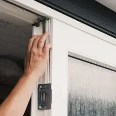 Hand justerar karmskruv på en vit dörr med frostat glas.