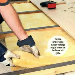 Händer med handskar lägger isolering med papp på ena sidan i ett golvbjälklag. Verktyg och golvbrädor ligger redo.