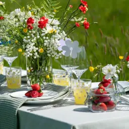 En vacker midsommar dukning med blommor, jordgubbar och glas med små gula blommor.