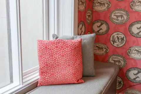 Färgglad tapetsera non woven med djurmotiv i ovala ramar. Två kuddar, en korallfärgad och en grå, vilar på en fönsterbänk.