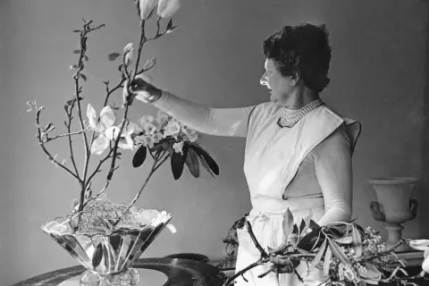 Constance Spry, en pionjär inom blomsterkonst, arrangerar magnoliagrenar och rhododendron i en elegant vas.