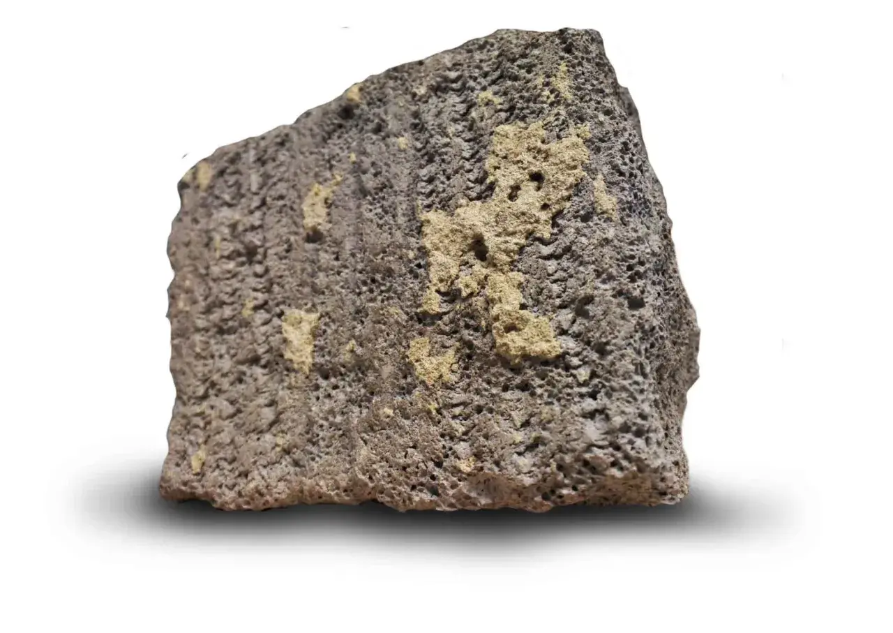 Ett stycke porös sten med mörkgrå och gulaktiga partier. Dess blåbetong utseende ger en känsla av naturlig textur.