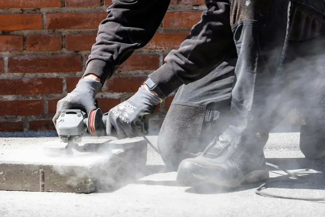 Person slipar betonggolv med vinkelslip. Damm virvlar upp runt arbetsytan.