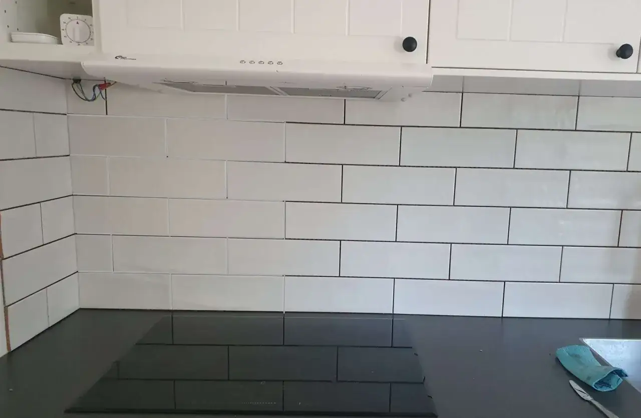 Vitt kakel med mörk fog i ett kök. En köksfläkt sitter ovanför kaklet. Kanske dags att måla fogar för en fräschare look?