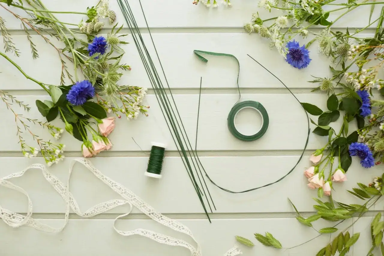 Förberedelser för att binda midsommarkrans med blommor, tråd och sidenband.