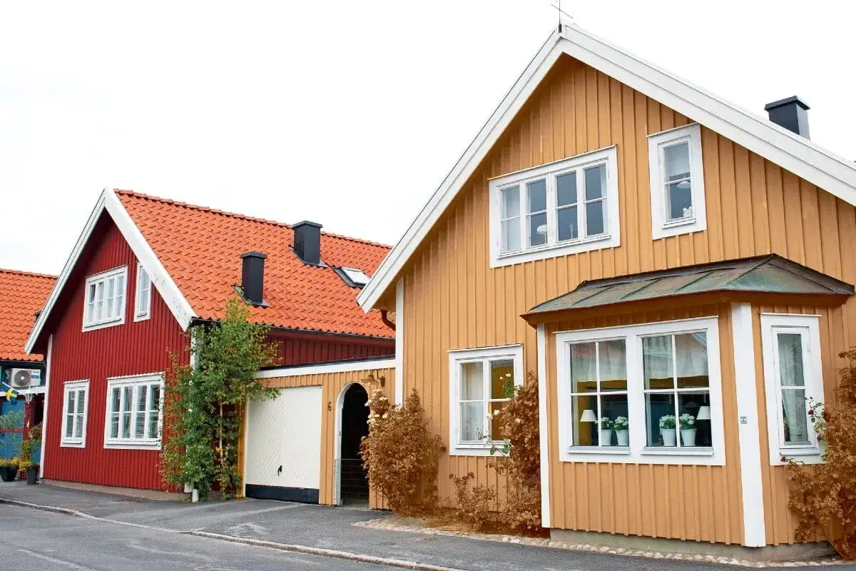 Två charmiga trähus, ett rött och ett gult, står sida vid sida. Kanske är det dags att måla huset för att fräscha upp fasaden.